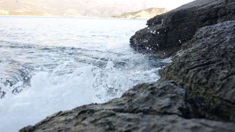 Waves-crashing-into-rocks-near-Budva-old-town-on-the-coastline-of-Montenegro-on-the-Adriatic-coastline-on-a-sunny-sunset-afternoon