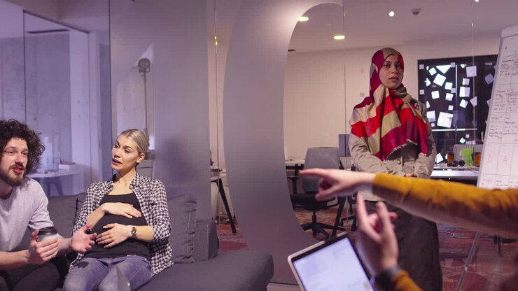 Donna musulmana in un moderno ufficio coworking open space che fa una presentazione al team. Donna d'affari araba mediorientale in un ufficio di startup creativo. Uomo d'affari disabile in sedia a rotelle a una riunione di team.