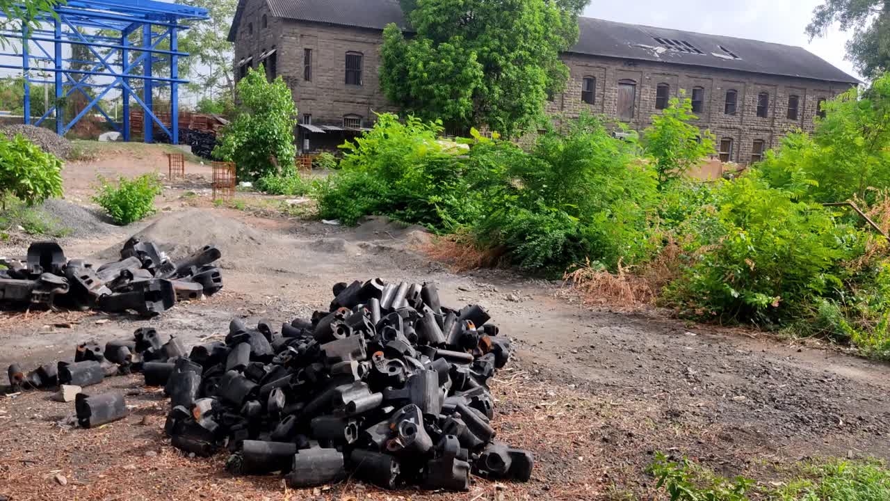 검은색 커플러 본체 조인트, 열차 보기용 너클 더미, 무성하게 자란 초목, 오래된 석조 사무실 건물이 배경으로 있는 산업 철도 야적장