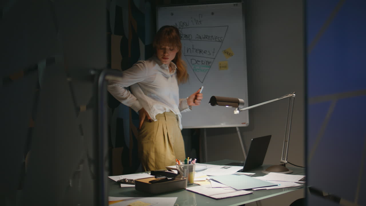 Joven empresaria trabajando hasta tarde en la oficina. Mujer seria mirando a la pizarra