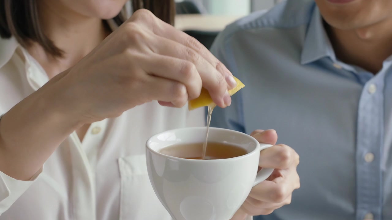En kvinne i hvit bluse tar frem en sitronbåt og klemmer saft i en tekopp på kontoret, for å smakssette teen.