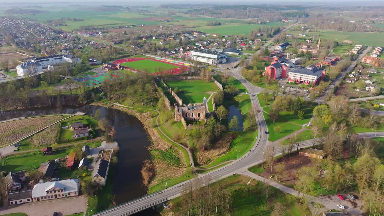 Historic Dobele Castle ruins nestled by the river and town in vivid green spring