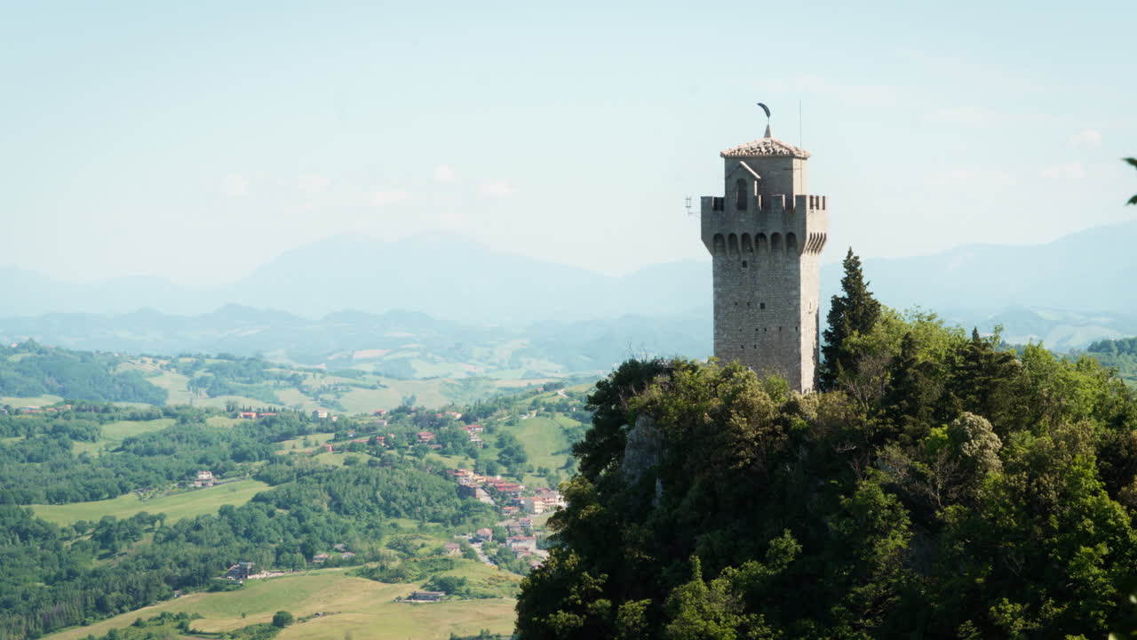 A mid-range shot of San Marino’s historic castle, perched on a mountain ridge and overlooking the rolling Italian countryside in the distance under a clear sky