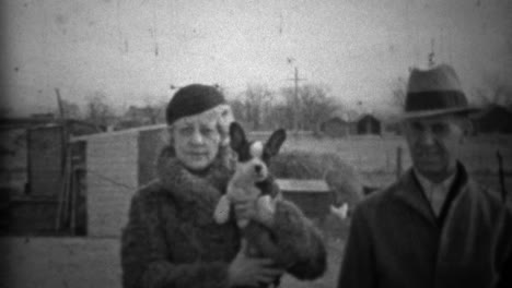 1933: couple showing off new small dog in formal winter clothing.