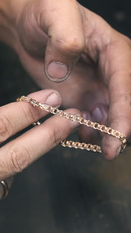 cu: professional goldsmith shows finished elegant gold bracelet over dark table in light jewelry workshop close view