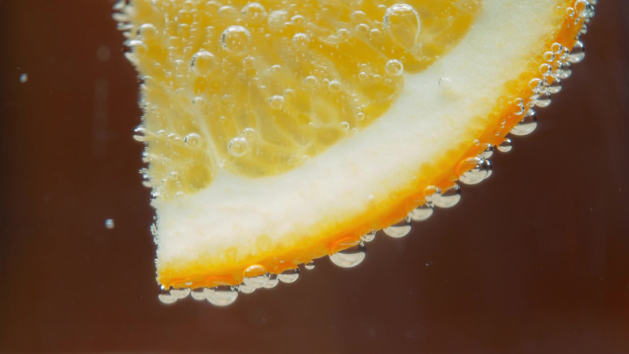 Primo piano di una fetta d'arancia in acqua frizzante con bolle d'aria.