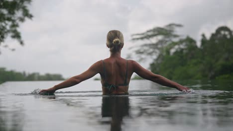 Elegante-Blonde-Frau,-Die-Im-Pool-Wirbelt-Und-Hände-Durch-Wasser-Spritzt,-Zeitlupe