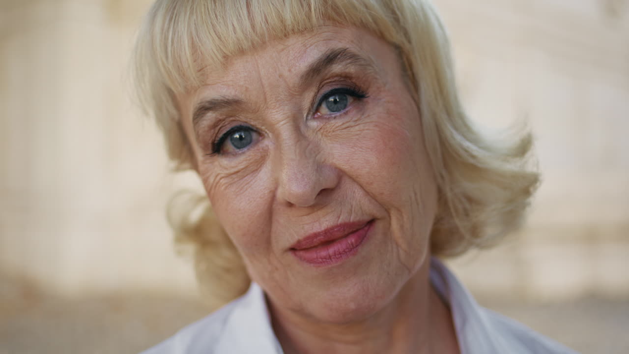 расслабленная старуха смотрит в камеру с нежной улыбкой на открытом воздухе крупный план. зрелая женщина