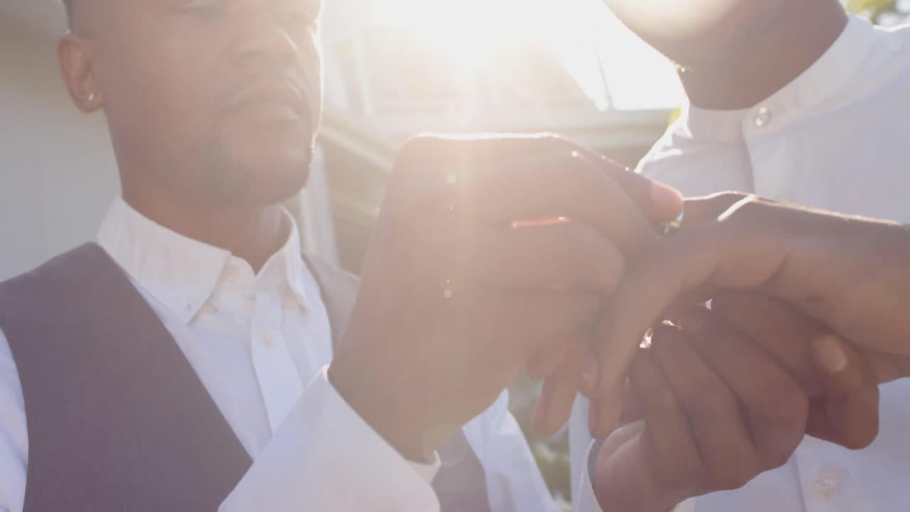 Happy african american gay male couple exchanging wedding rings, slow motion