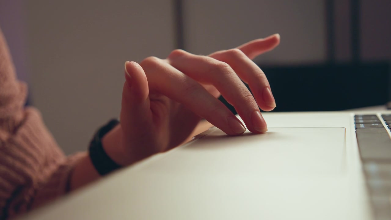 Primo piano di una mano destra che aleggia sopra la tastiera di un laptop, con i polpastrelli curvi e leggermente abbassati, che mostra un movimento di digitazione pronto o un leggero tocco con un sottile movimento delle dita in un ambiente di lavoro interno caldo.