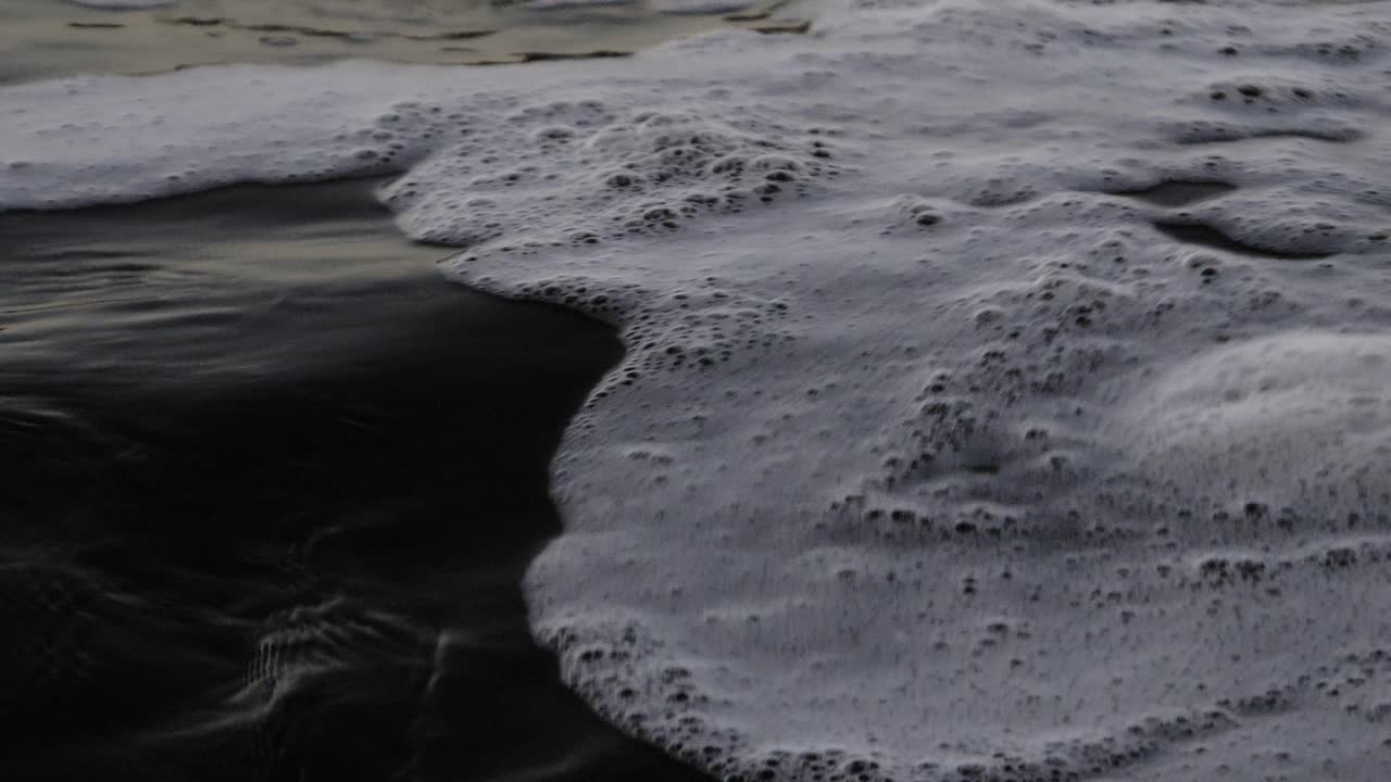 Close-up of sea foam on the shore with details of bubbles. Slow motion.