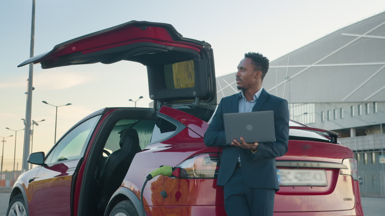 hombre de negocios usando una computadora portátil al lado de un coche eléctrico