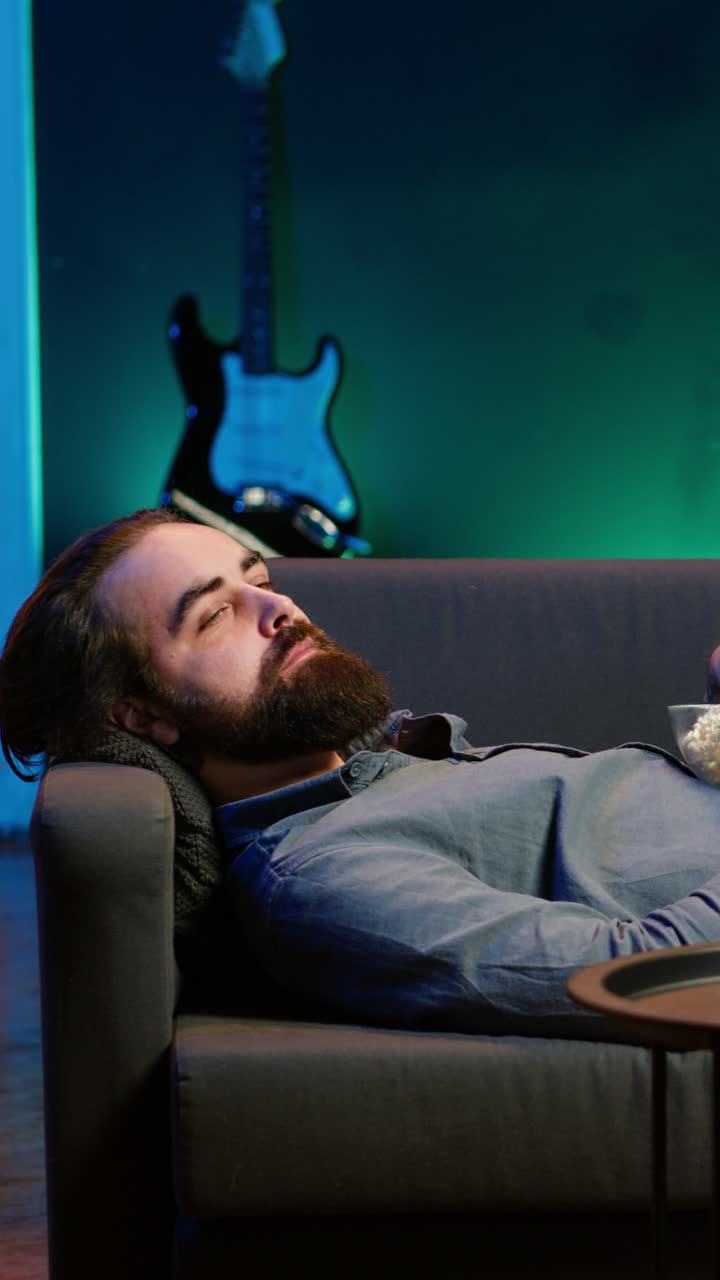 Vertical video Upbeat homeowner laying down on couch watching feel good movies on TV