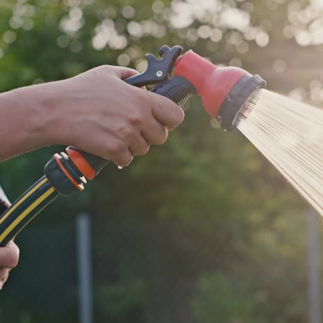 the gardener's hand waters with a garden hose using a water gun