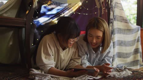 asian mother and daughter smiling while using digital tablet under blanket fort at home