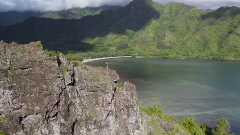 incredible aerial drone pov with natural parallax perspective of people on top of dangerous cliff on crouching lion hike with breathtaking view of kahana valley and bay, hawaii