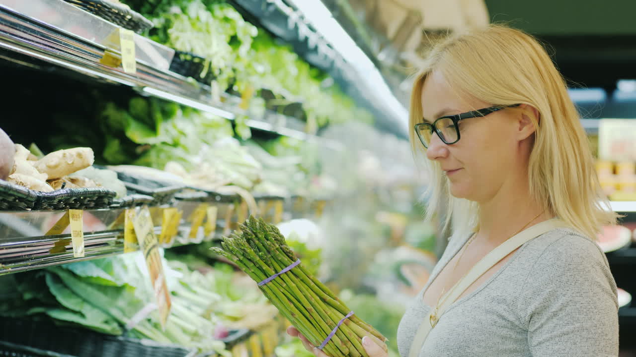 중년 여성은 슈퍼마켓 야채 부서에서 채소를 선택합니다.