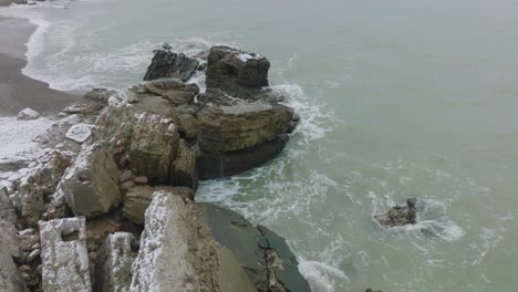 Aerial-birdseye-view-of-abandoned-seaside-fortification-buildings-at-Karosta-Northern-Forts-on-the-beach-of-Baltic-sea-,-overcast-winter-day,-drone-shot-moving-forward,-tilt-down