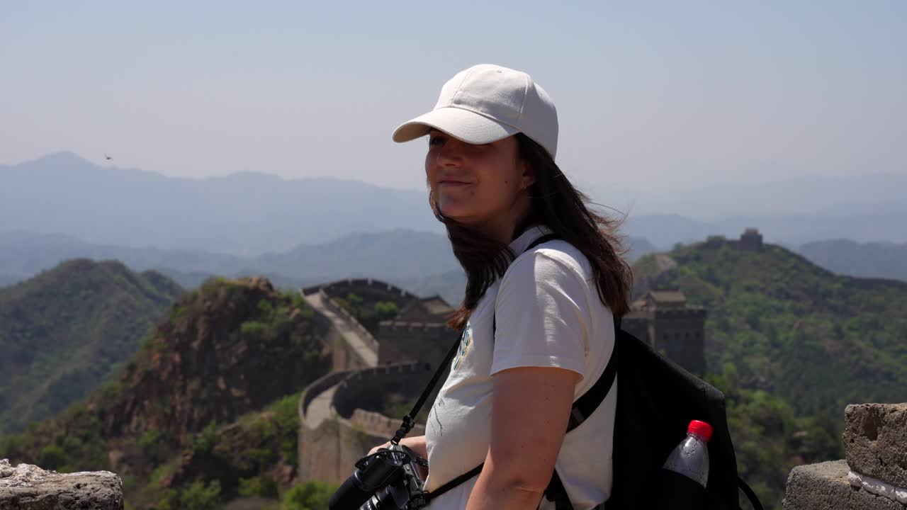 una mujer sonriente sostiene una cámara, abrazando la brisa en la cima de la gran muralla. beijing, china