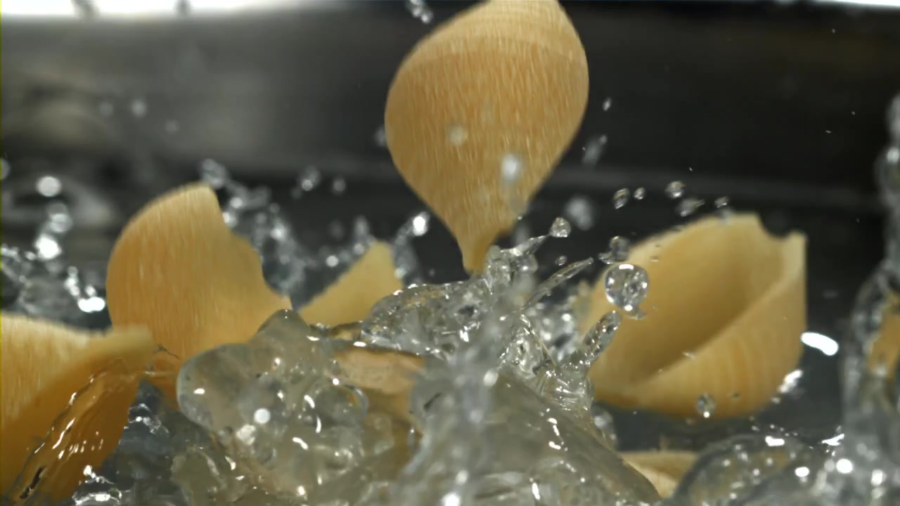 Nudelschalen fallen in Zeitlupe in kochendes Wasser