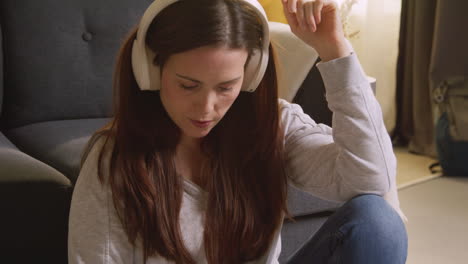 woman wearing wireless headphones sitting on floor at home streaming music from mobile phone 6