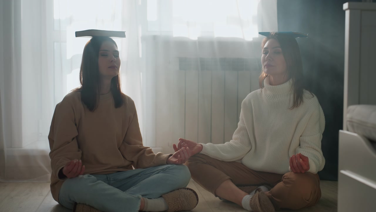 Mulher equilibrando livro na cabeça enquanto recebe orientação de gramática em casa, luz solar suave filtrando pelas cortinas realça expressão focada, sentada de pernas cruzadas no chão vestindo suéteres de tricô.