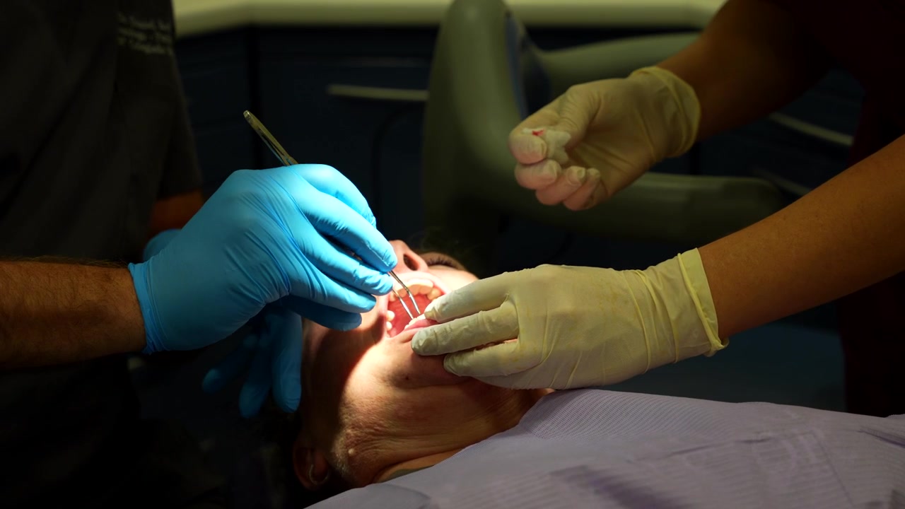 Dentista removendo ponto da boca do paciente com assistente limpando instrumentos