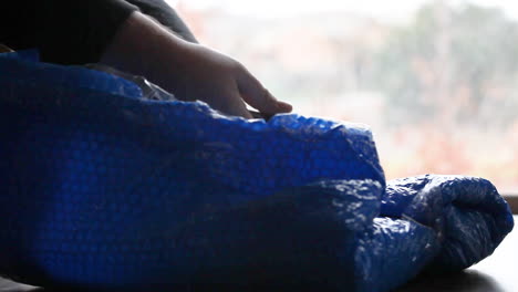 male hands using cutting knife to open blue bubble wrapped delivery.