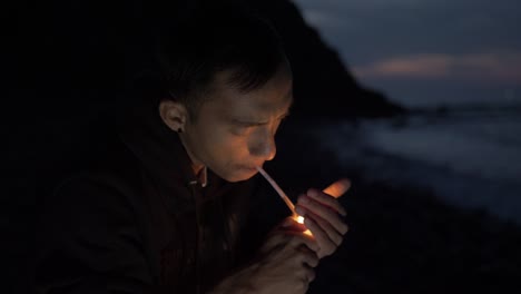 young nepalese man sitting alone on beach at night lighting cigarette