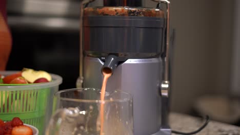 exprimidor eléctrico de primer plano con boquilla que vierte jugo de fruta saludable y vívido en una jarra de vidrio - aparato de cocina exprimidor eléctrico que hace jugo de fruta fresco saludable - enfoque selectivo de primer plano - dieta exprimidora
