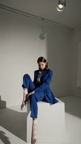 woman in blue suit sitting on a cube in a studio