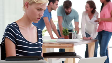 Casual-businesswoman-working-on-laptop-while-her-colleagues-having-meeting