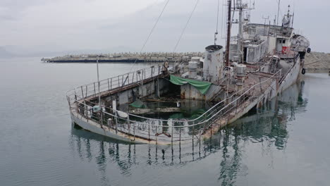 Rusty-grey-half-submerged-shipwreck-anchored-near-the-shore-on-a-cloudy-overcast-day