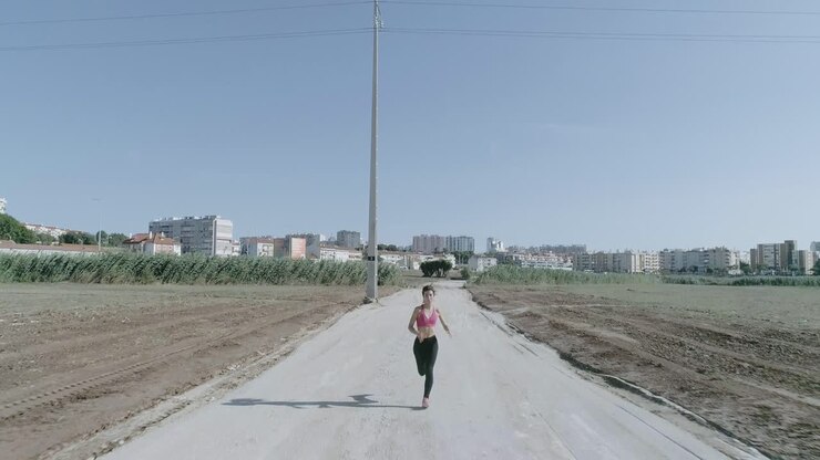 Ampia ripresa con drone di una giovane donna che corre al rallentatore verso la telecamera su una strada sterrata in un parco urbano