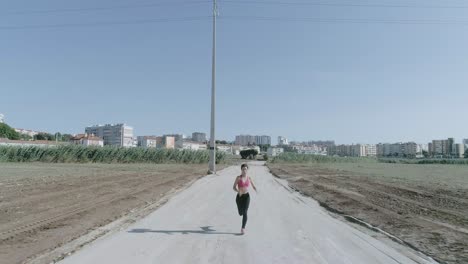 amplia toma de drone de una joven corriendo en cámara lenta hacia la cámara en un camino de tierra del parque urbano