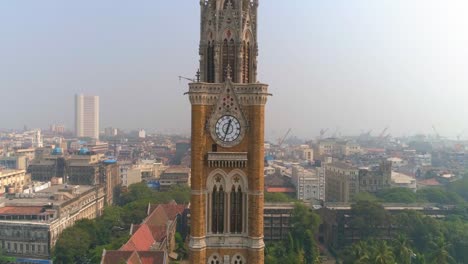 drone shot of the rajabai clock tower next to the bombay high court building and oval maidan, an ornate 1878 clock tower modeled after big ben and featuring stained-glass windows and musical chimes