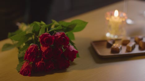 와인과 초콜릿으로 집에서 낭만적인 발렌타인 데이를 위해 테이블에서 장미 다발을 줍는 남자