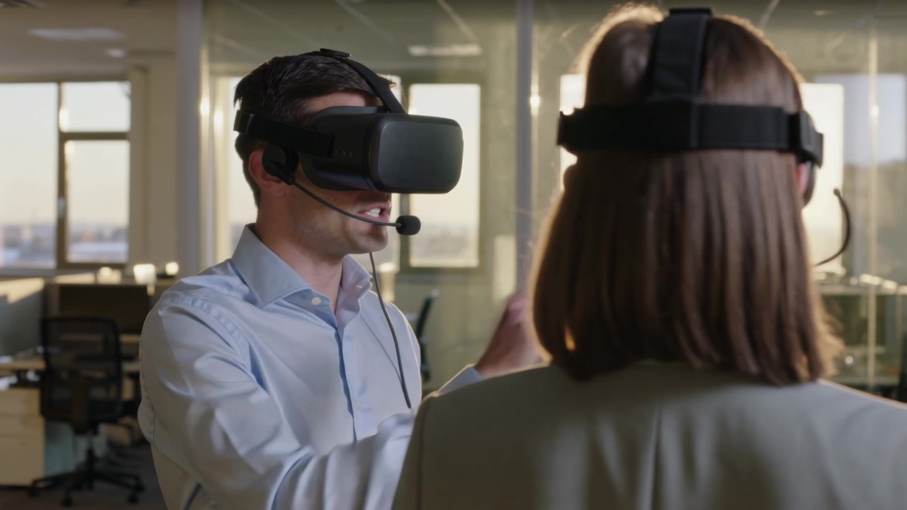 Tecnico che parla in camicia blu, calibra un visore VR su una donna in una demo d'ufficio, con cavo del microfono a braccio.
