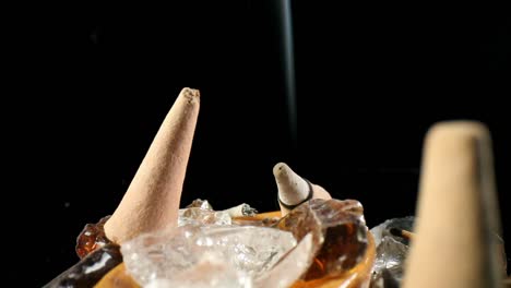 Static-shot-of-unlit-incense-cone-and-one-lit-in-a-decorative-rock-garden,-smoke-rolling-in-the-back