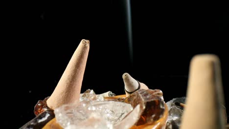 static shot of unlit incense cone and one lit in a decorative rock garden, smoke rolling in the back