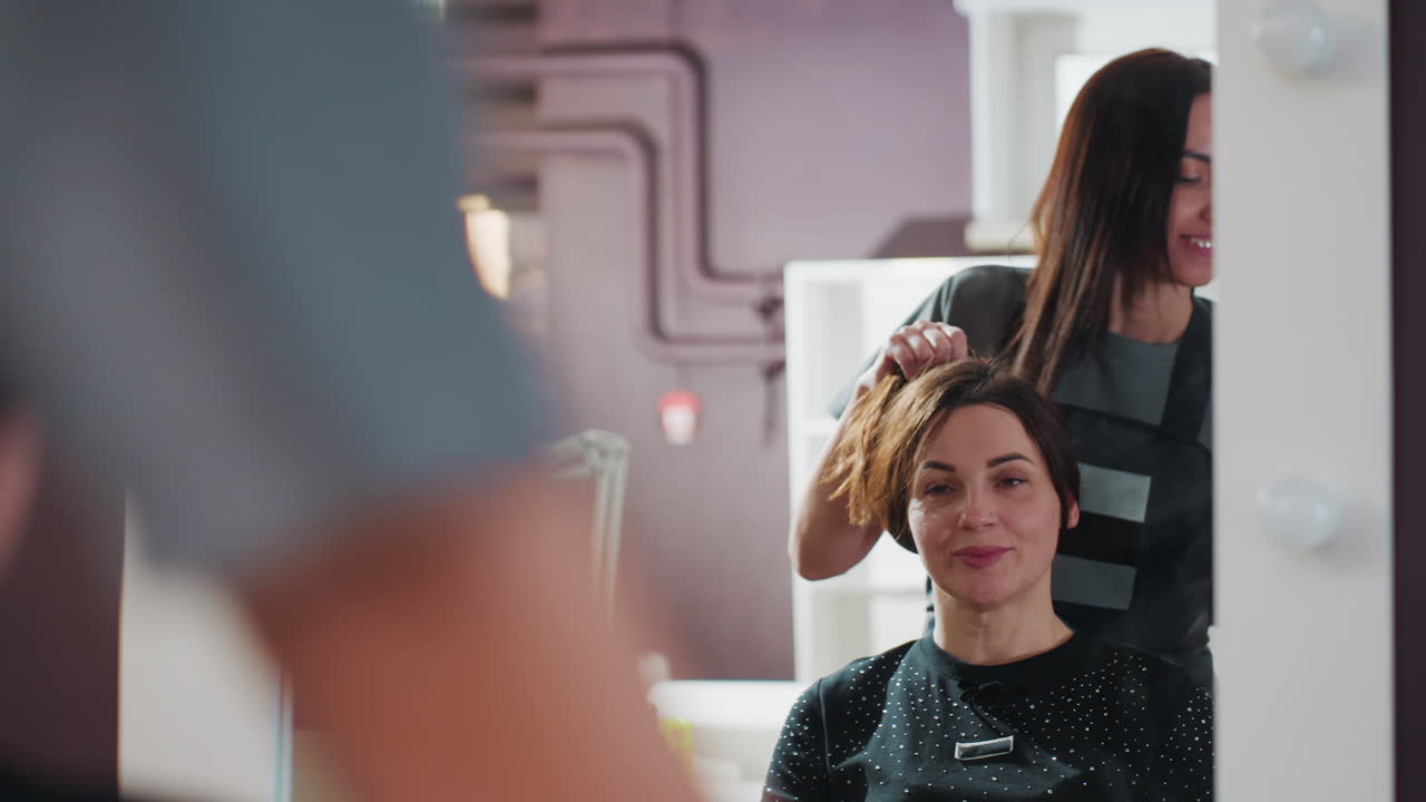 Cliente sonriente esperando en la peluquería, señora disfrutando de una sesión de belleza en un salón contemporáneo, mujer caucásica relajándose mientras el peluquero la prepara para el corte de pelo en un entorno elegante.