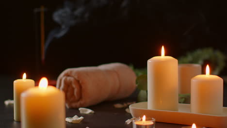 vida muerta de velas encendidas con bastón de incienso de planta verde y toallas suaves contra un fondo oscuro como parte de la relajante decoración del día de spa 2