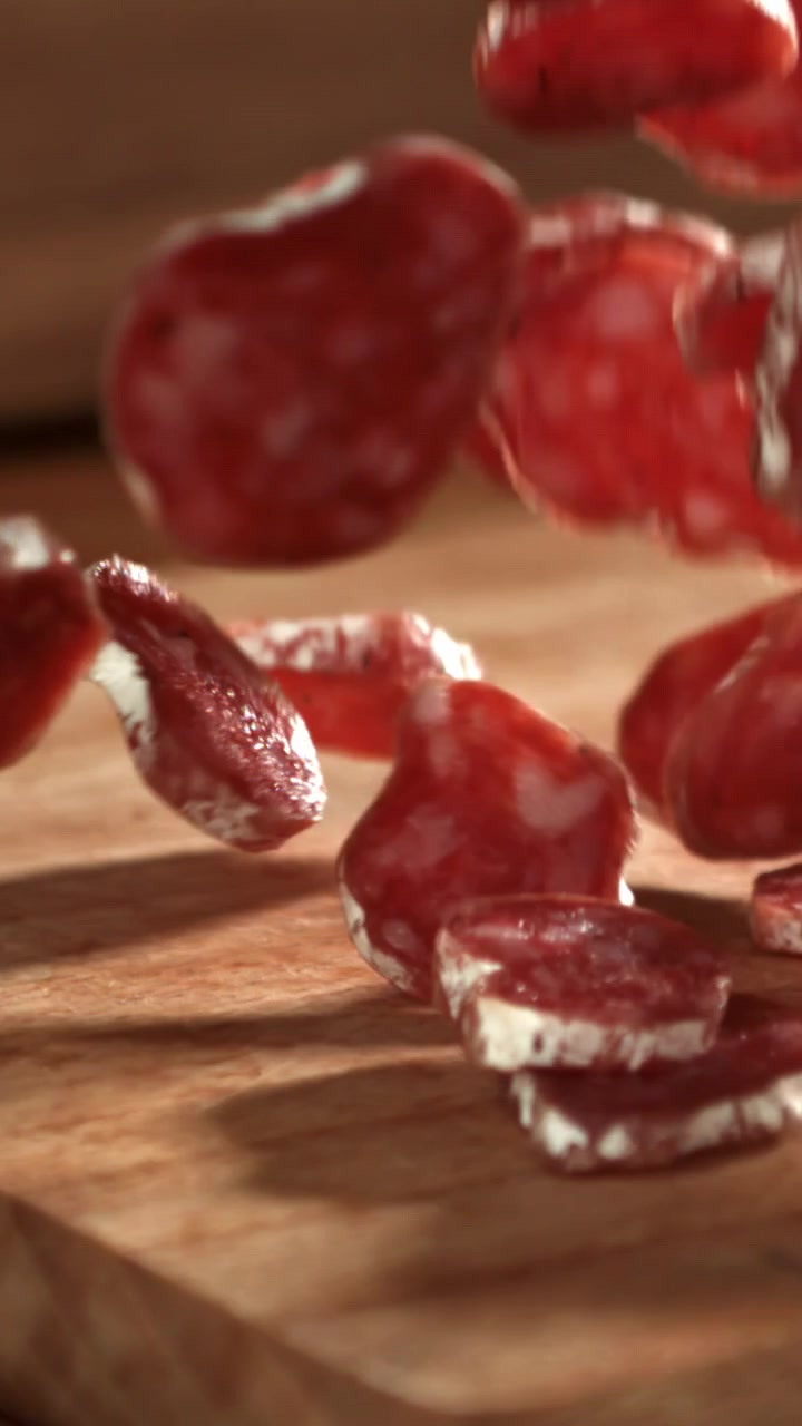 Fette di salame che cadono su un tagliere di legno al rallentatore