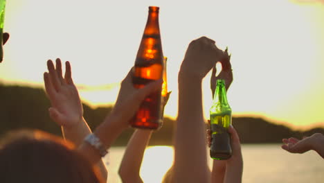 los adolescentes están bailando con las manos en alto con cerveza. esta es la fiesta perfecta al atardecer en la costa del lago.