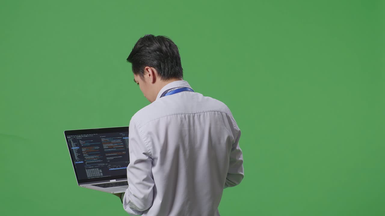 스튜디오에서 녹색 화면 배경에서 노트북 컴퓨터를 사용하는 아시아 사업가의 뒷면, 컴퓨터 디스플레이 코드를 보여줍니다.