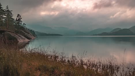 Strahlen-Der-Untergehenden-Sonne-Scheinen-Durch-Die-Stürmischen-Wolken,-Die-über-Dem-See-Und-Einem-Wald-In-Einem-Zeitraffervideo-Wirbeln