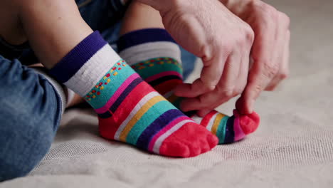 adult helping a child put on colorful striped socks