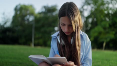 a young woman sits on the grass in a park and writes in a notebook