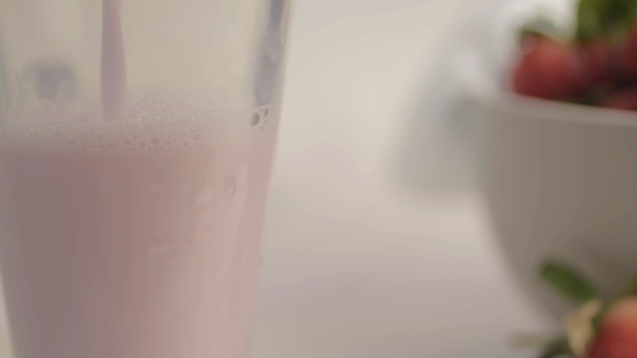 Versare un fresco frappè alla fragola spumoso in un bicchiere, primo piano