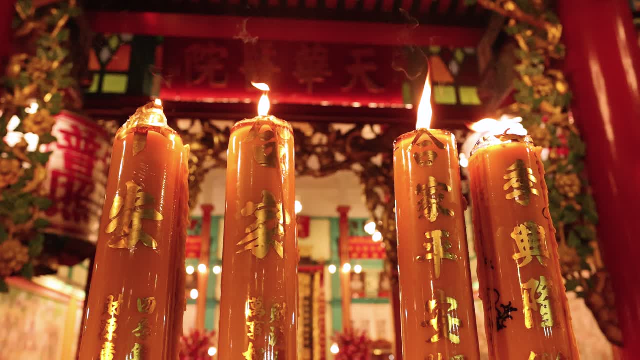 Tall orange candles burn steadily in ornate temple, warm lighting, slight camera movement, nighttime ambiance